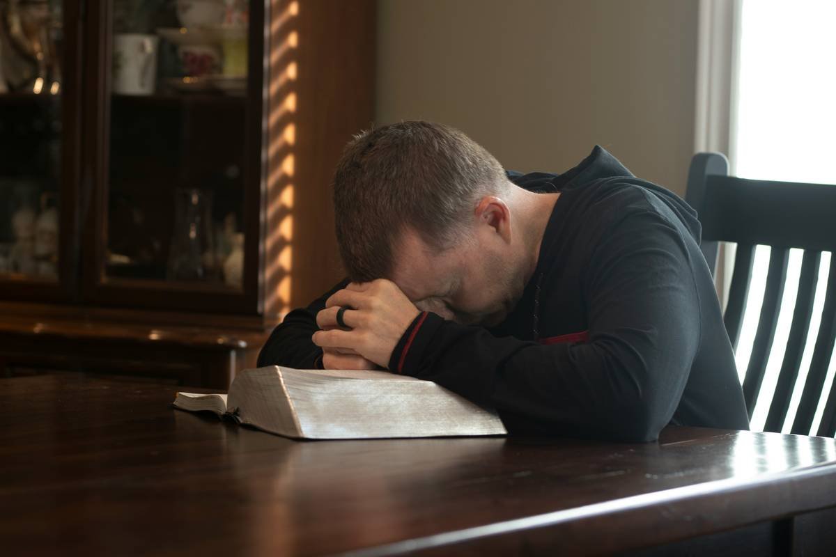 Man praying with his hands on Bible