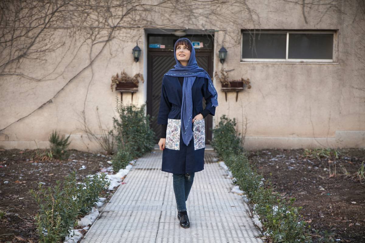 woman in purple jacket standing on gray concrete pathway