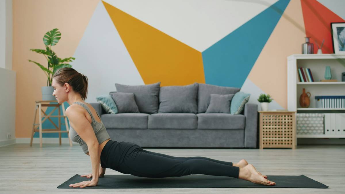 Healthy young woman is doing complex of yoga asanas at home on comfortable mat developing stamina and flexibility. People and modern sports concept.